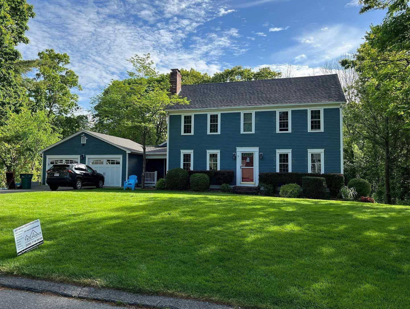 Blue house with attached garage, set on a grassy lawn, under a blue sky.