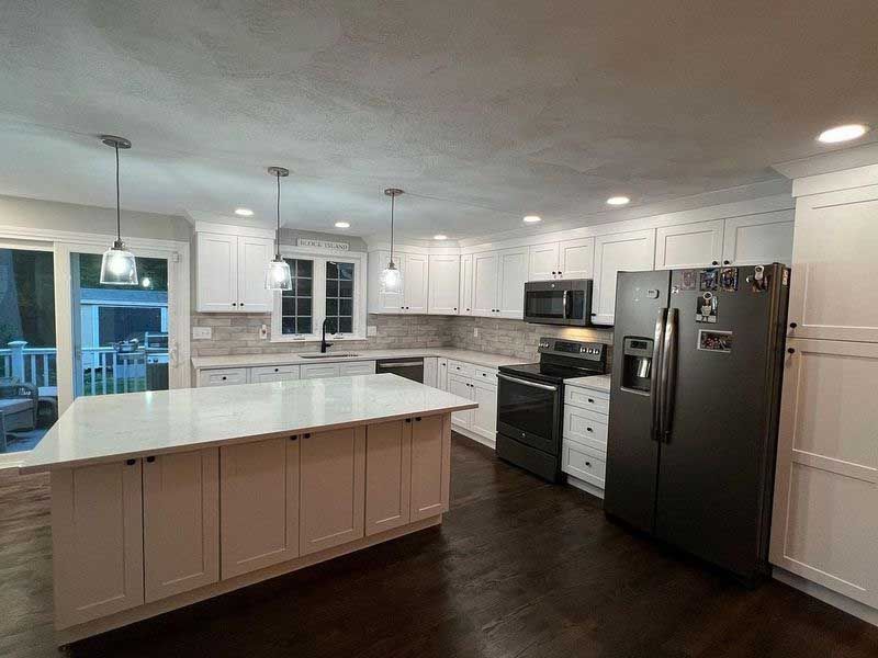 White kitchen with island, black appliances, and dark wood floor.