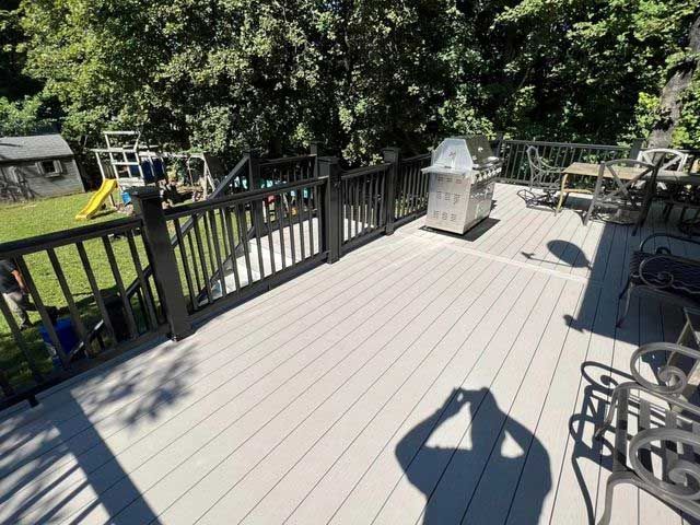 Spacious gray deck with black railing; a grill, chairs, and a playground are visible.