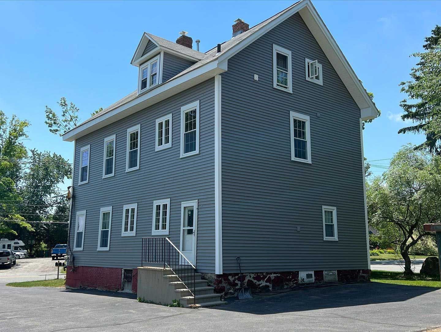 Gray multi-story house with white window frames and a small staircase leading to the entrance. Sunny day.