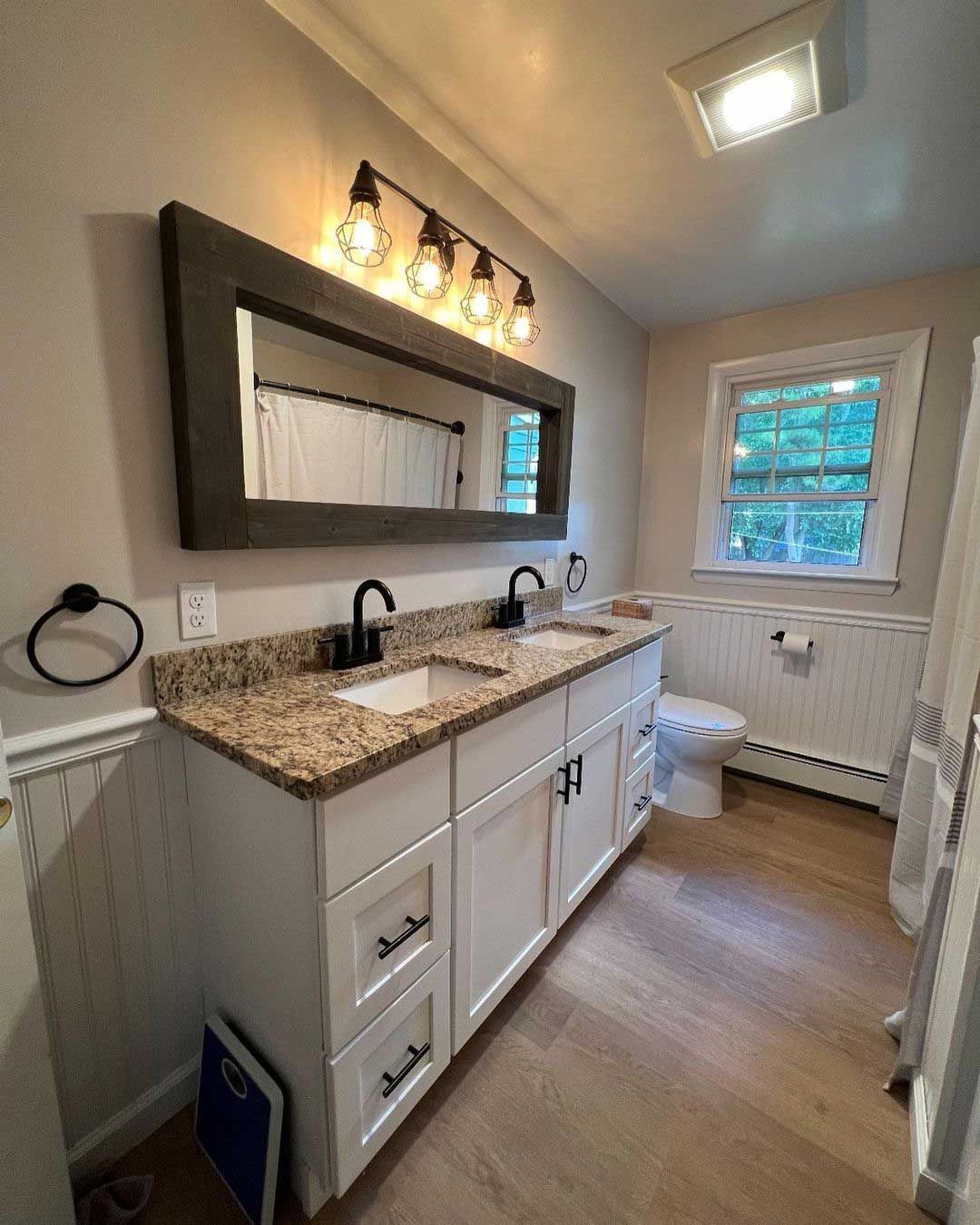 Bathroom with white vanity, granite countertop, black fixtures, large mirror, and window.