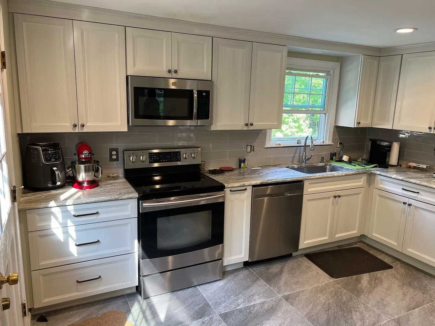 White kitchen with stainless steel appliances, gray backsplash, and granite countertops.