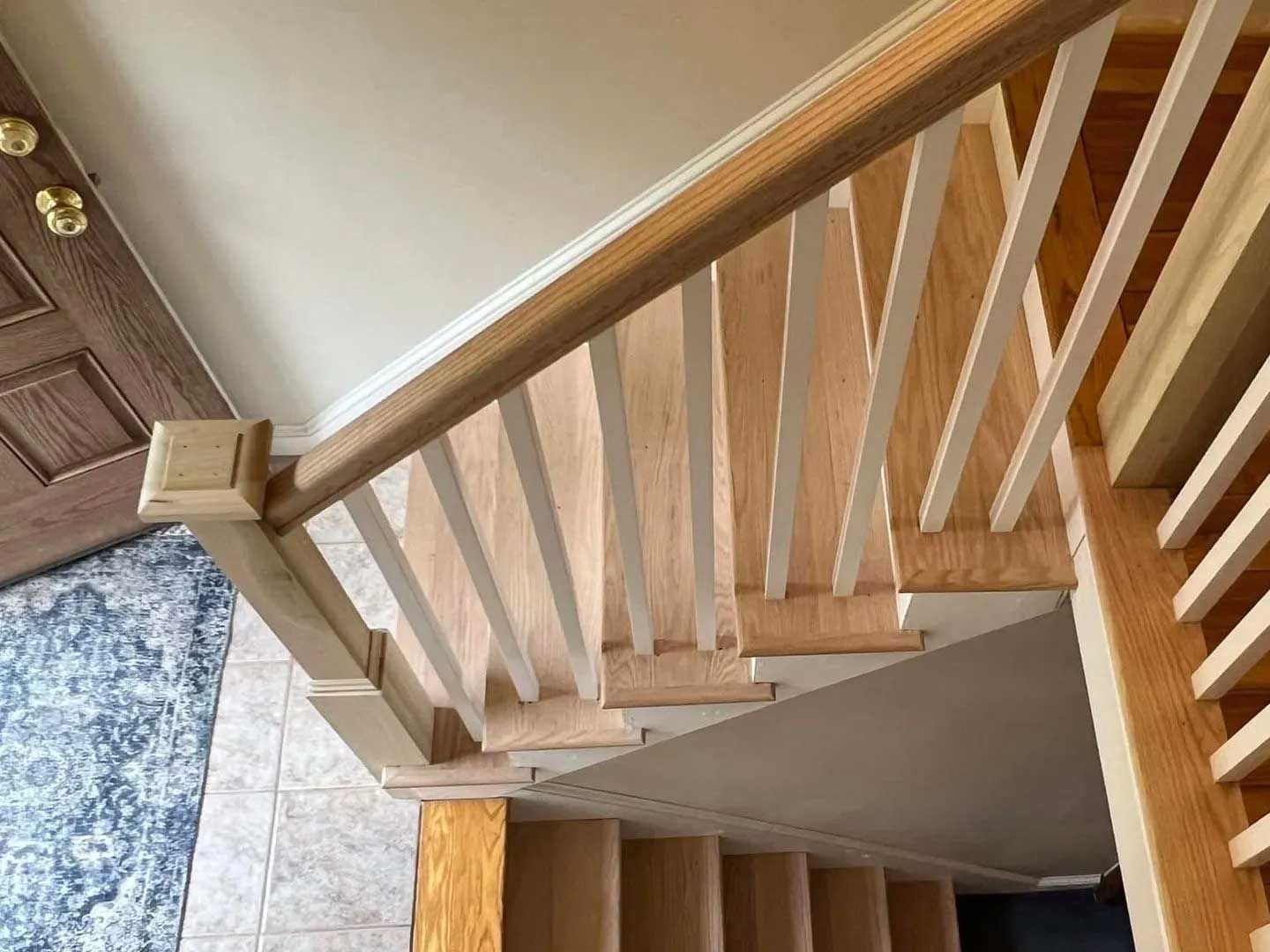 Staircase with wooden handrail and white spindles. Light wood steps lead down to a landing.