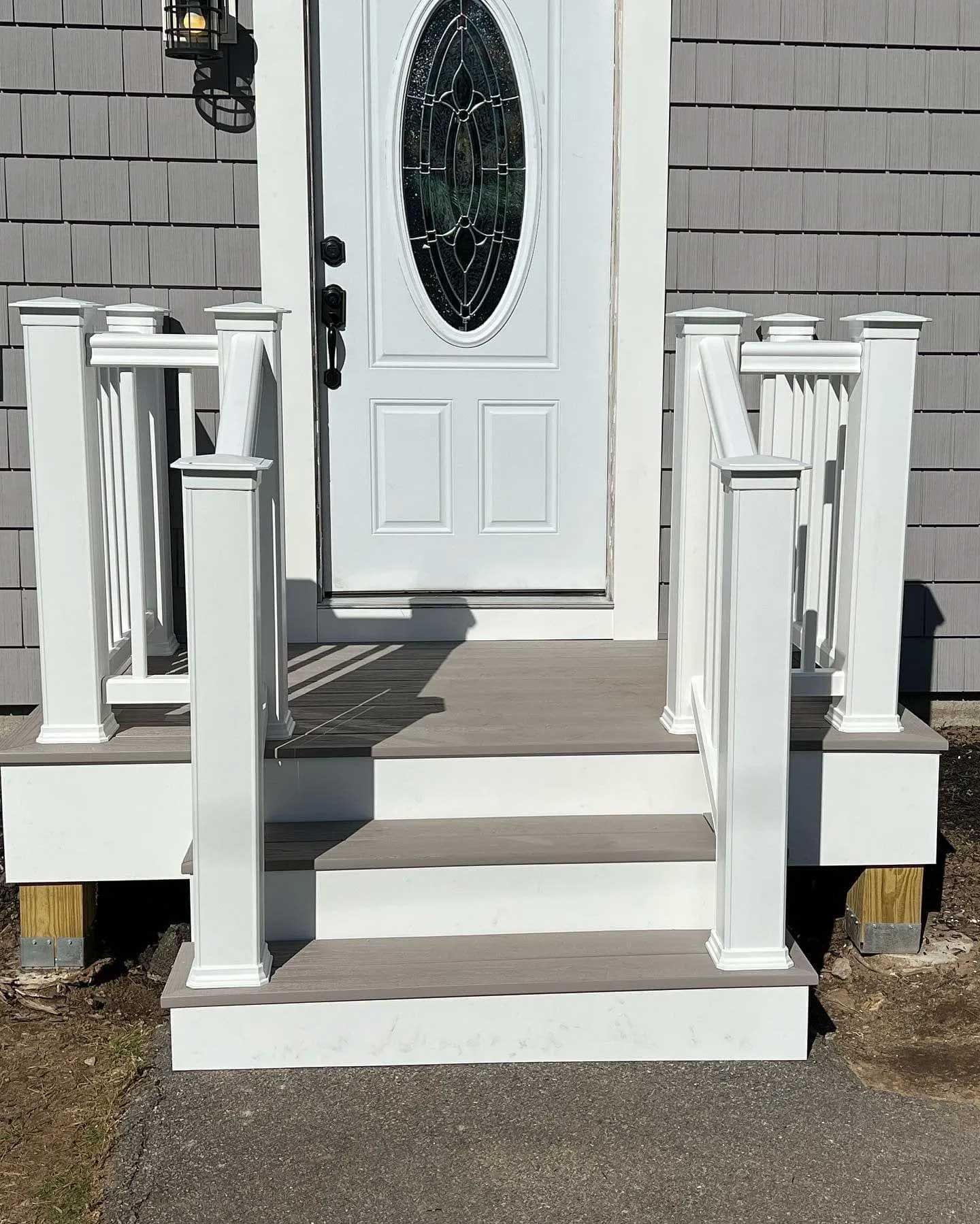 White door with oval window, grey steps, and white railings.