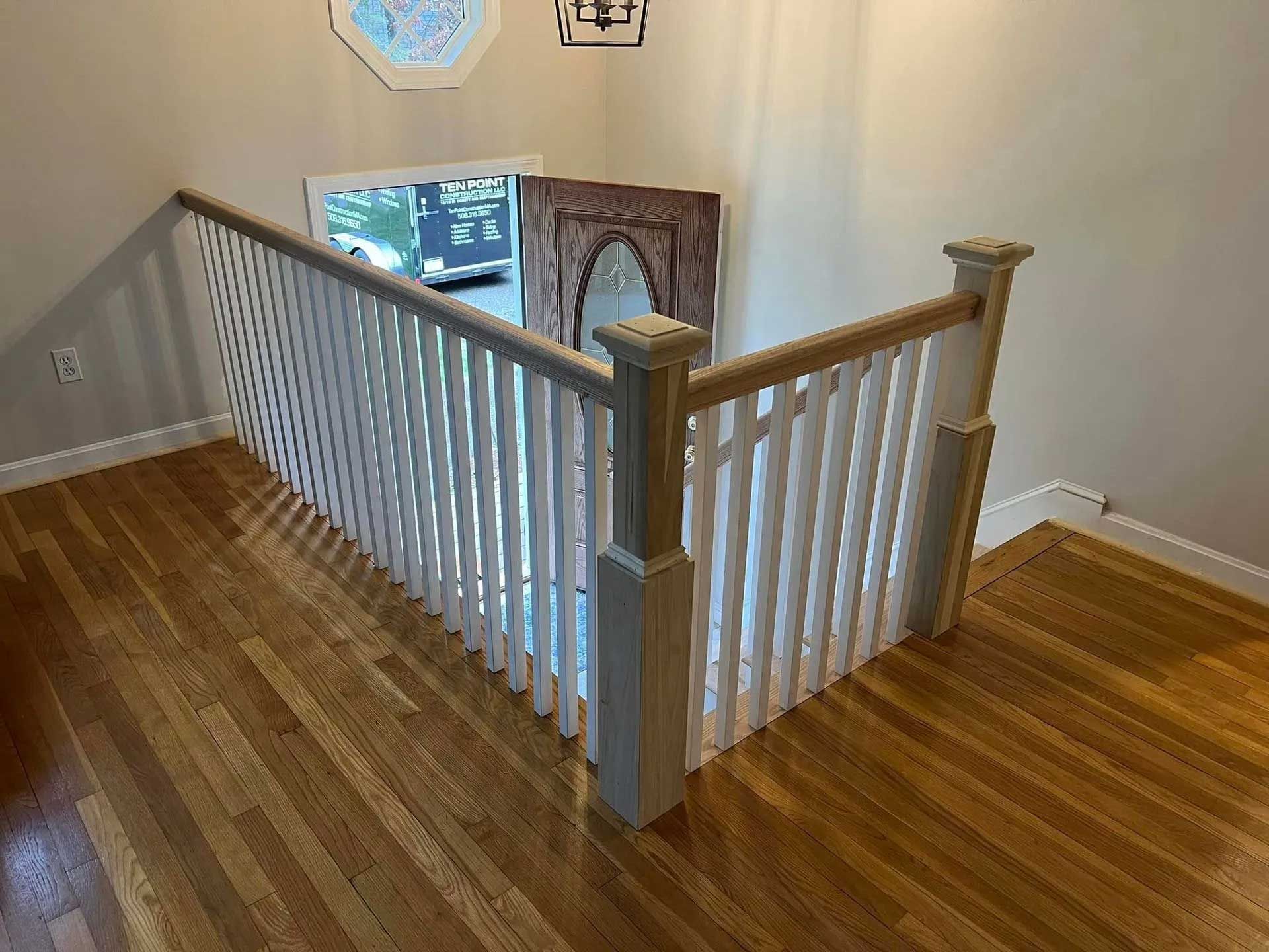 Wooden staircase with white banister, viewed from above.
