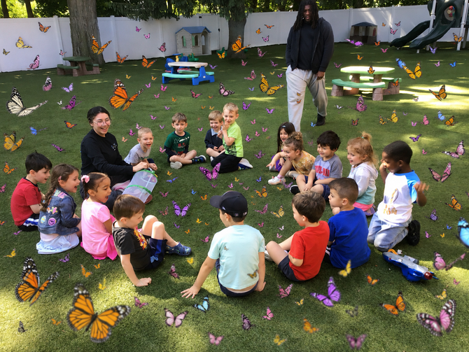 Children in a classroom pose with a rainbow art project.