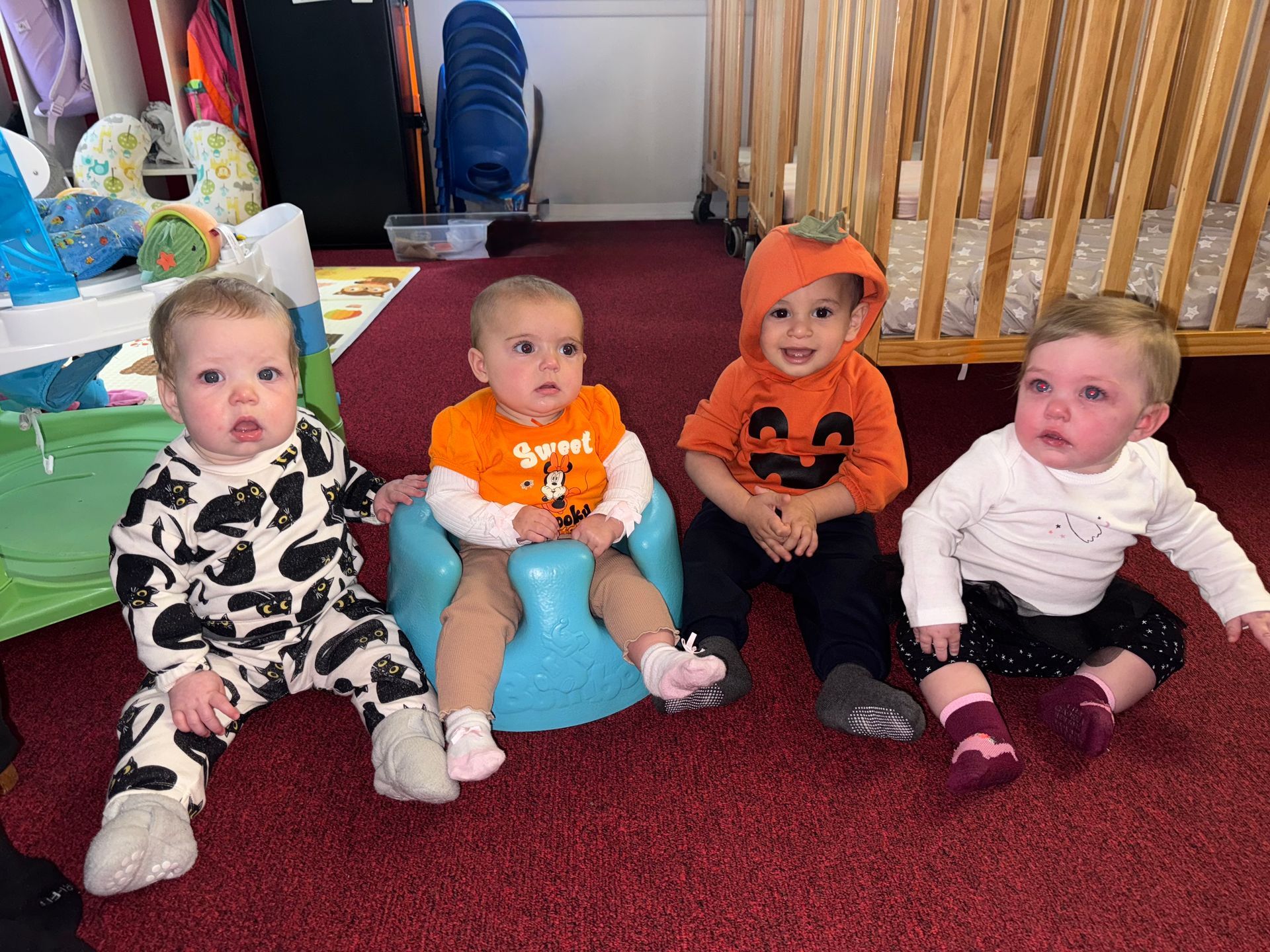 Children in a classroom pose with a rainbow art project.