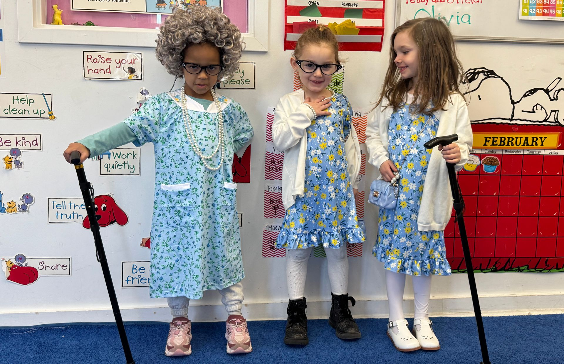Children in princess costumes stand in front of a decorated wall; a cardboard castle is in front.