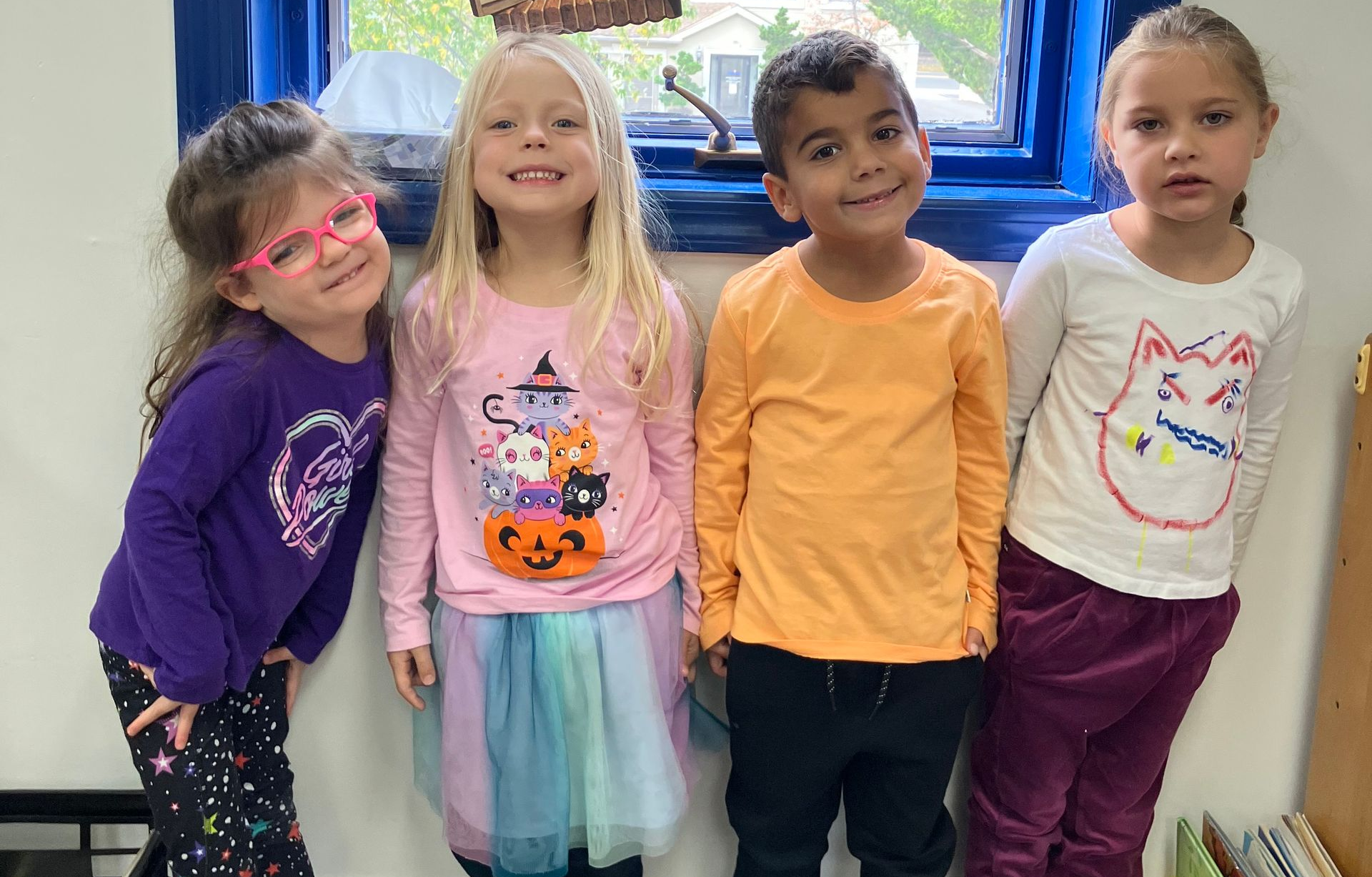 Group of children wearing apple shirts, posing in a classroom, with apple tree cutouts.
