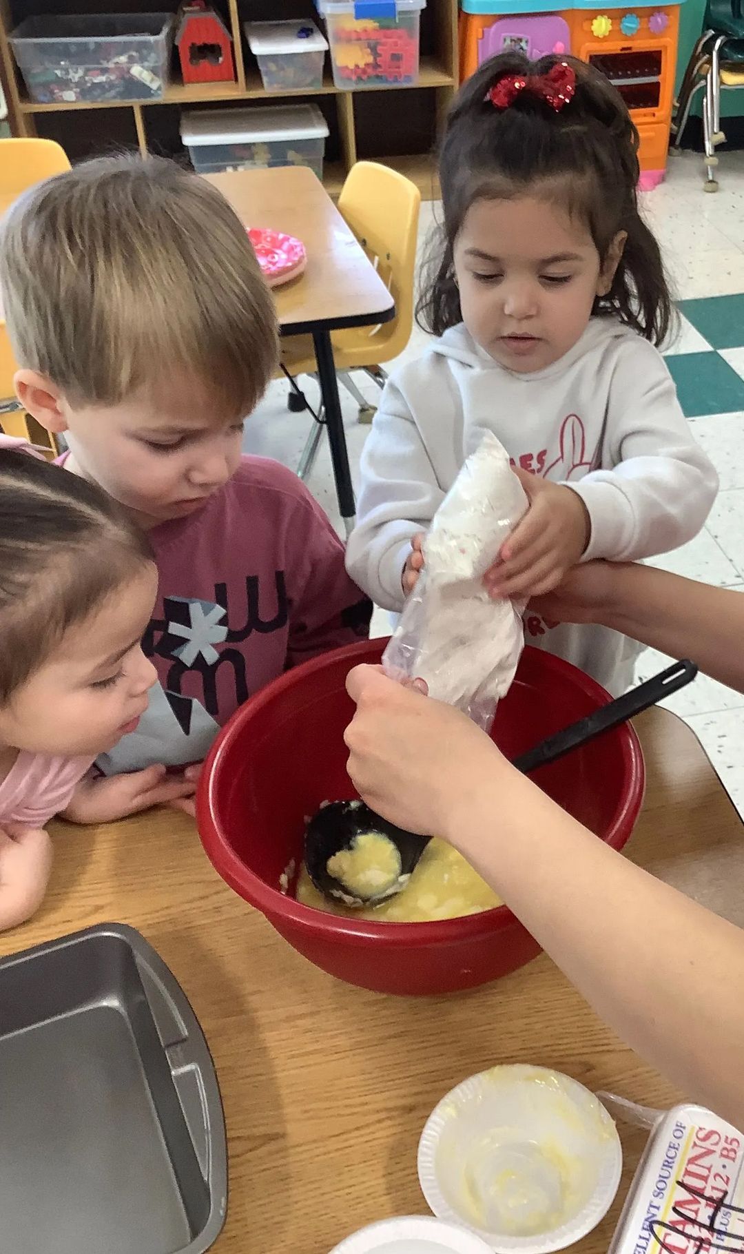 Children adding ingredients to a bowl while baking, indoors.