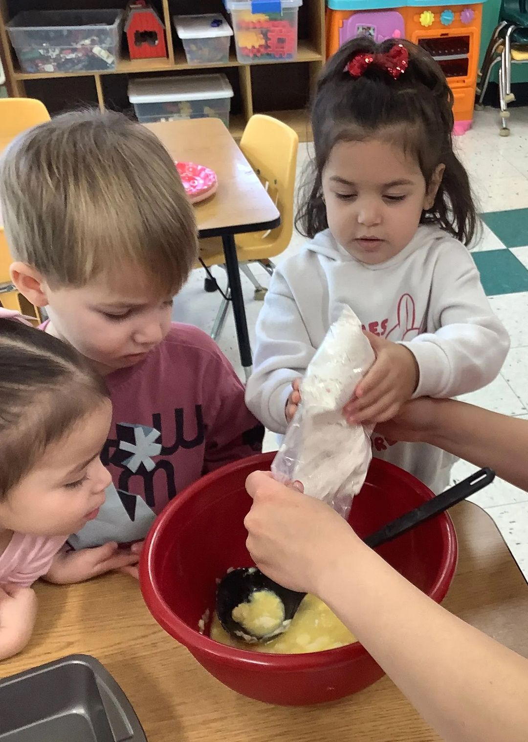Children adding ingredients to a bowl while baking, indoors.