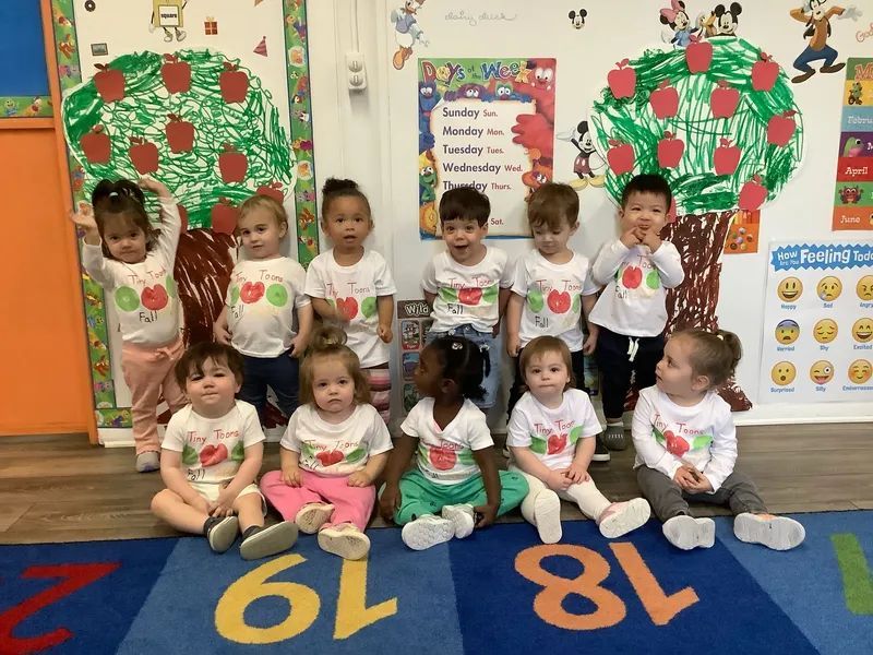 Group of children wearing apple shirts, posing in a classroom, with apple tree cutouts.
