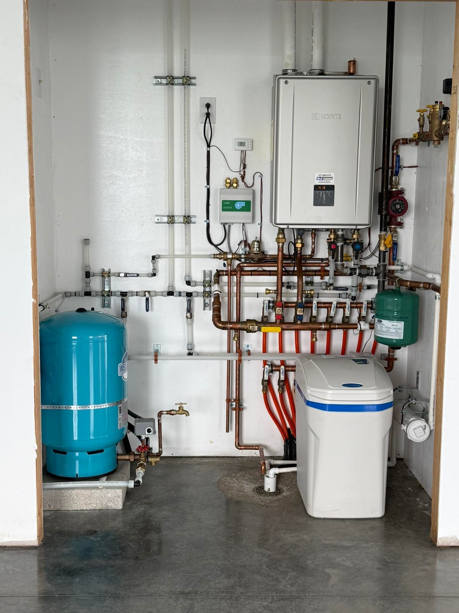 A utility room with a blue water tank, white water softener, and heating system with copper pipes.