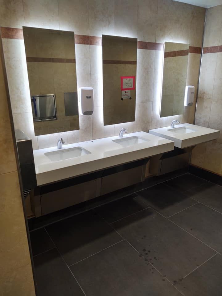 Public restroom with three sinks and mirrors, featuring a neutral color palette and overhead lighting.