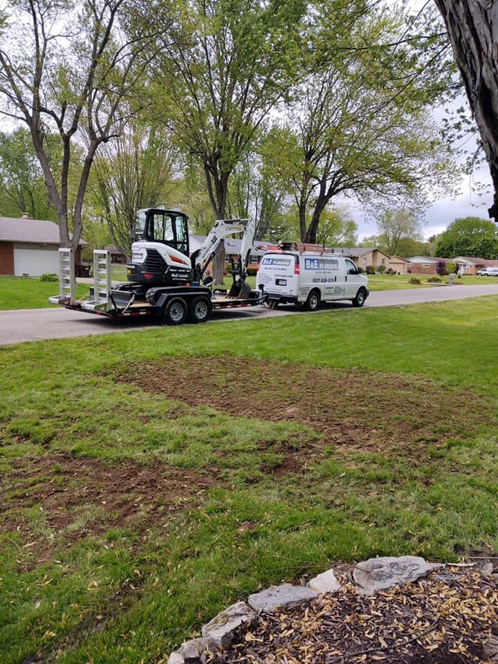 An excavator on a trailer and a white van parked on a grassy lawn.