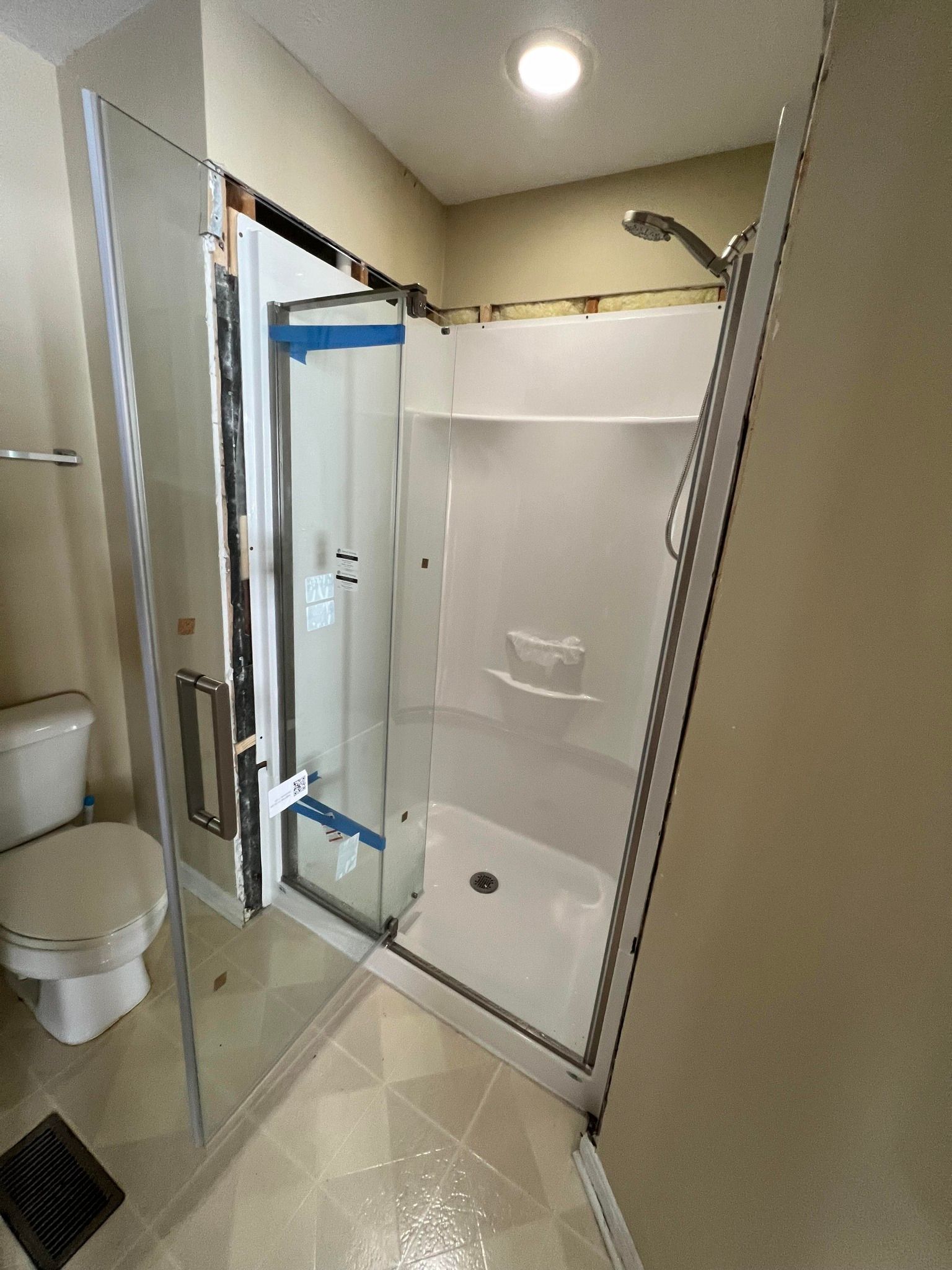 A bathroom with a clear glass shower, toilet, and beige walls. The shower door is ajar.