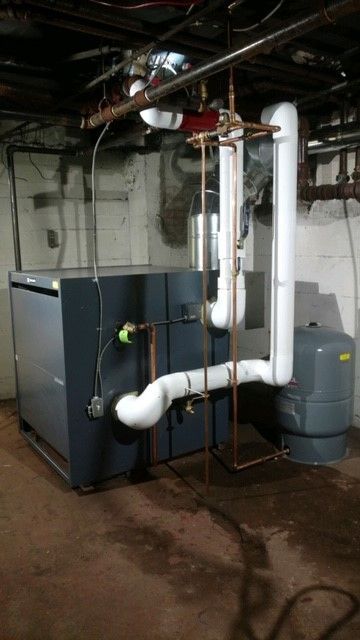 A large, gray furnace with copper and insulated pipes in a basement.