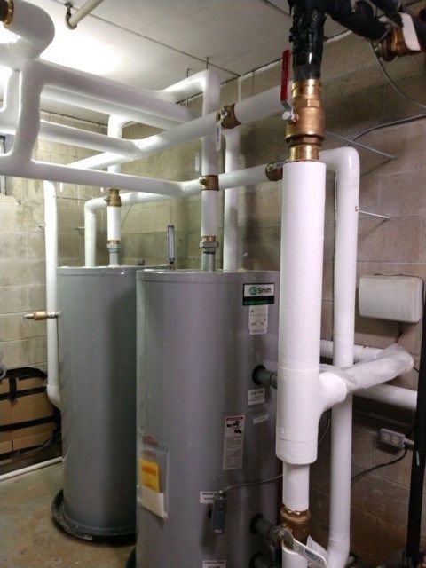 Two large gray water heaters with white insulated pipes in a utility room.