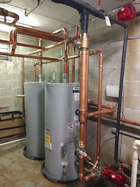 Two large gray water heaters with copper pipes against a concrete wall, likely an industrial setting.
