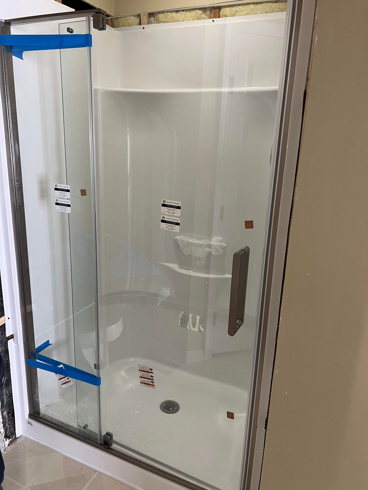 A glass shower enclosure with a white interior, viewed from outside. Blue tape is on the door.