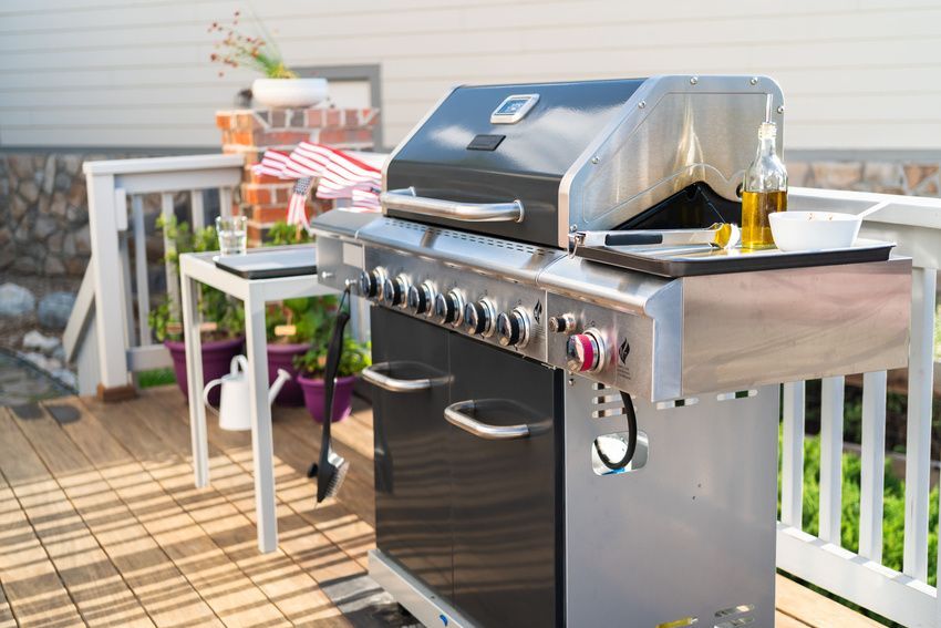 Gas grill on a wooden deck, ready for cooking, with oil and bowl.