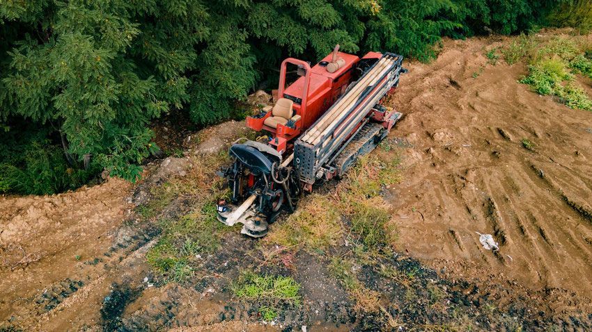 Red horizontal directional drilling machine in a field near trees.
