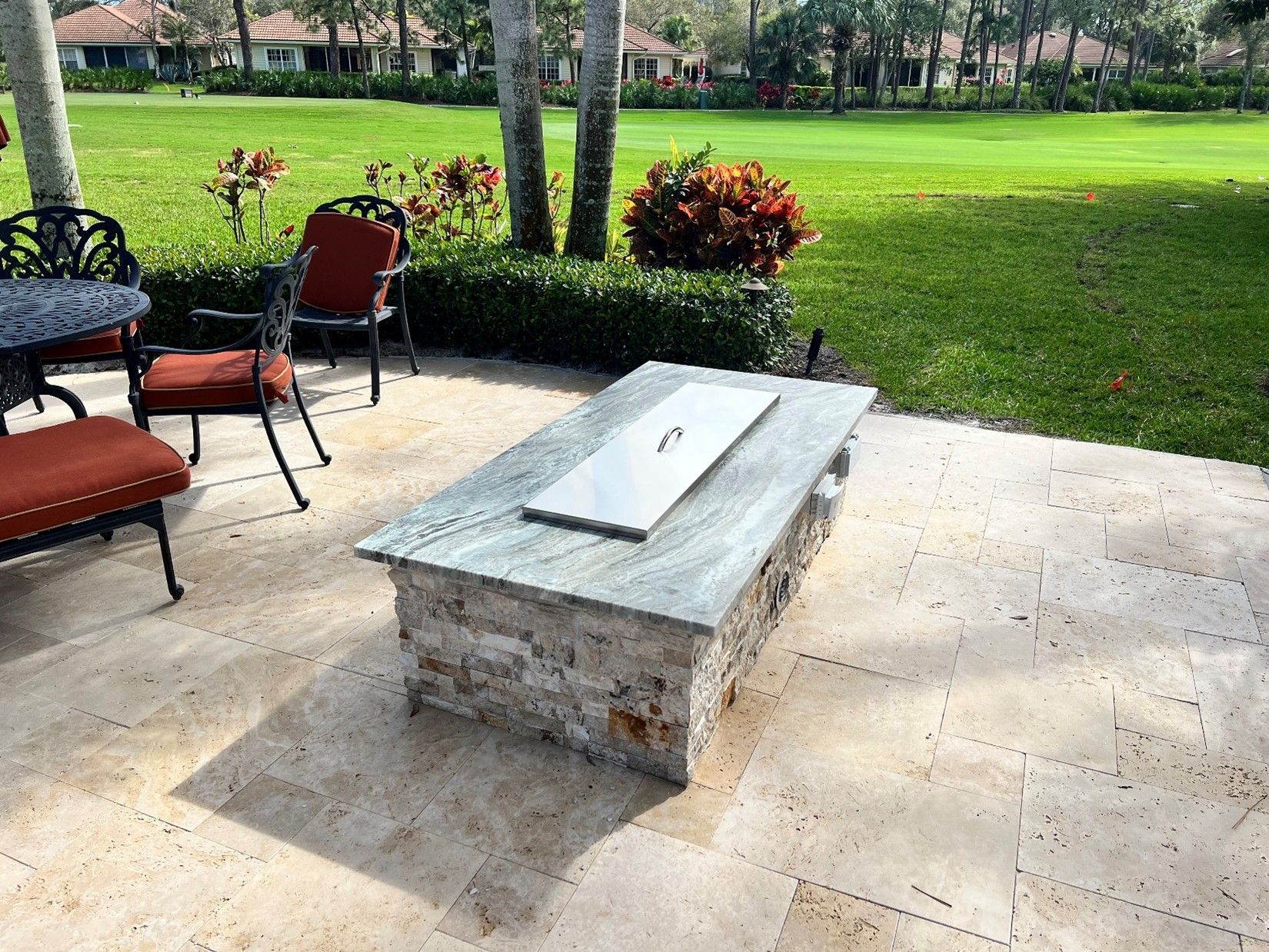 Stone outdoor bench with a white cushion on a patio beside chairs and a grassy lawn