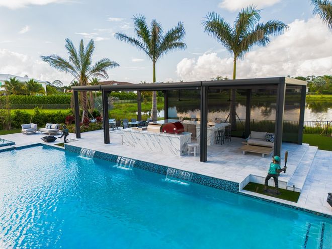 Modern backyard pool with a glass cabana, lounge chairs, and palm trees under a blue sky