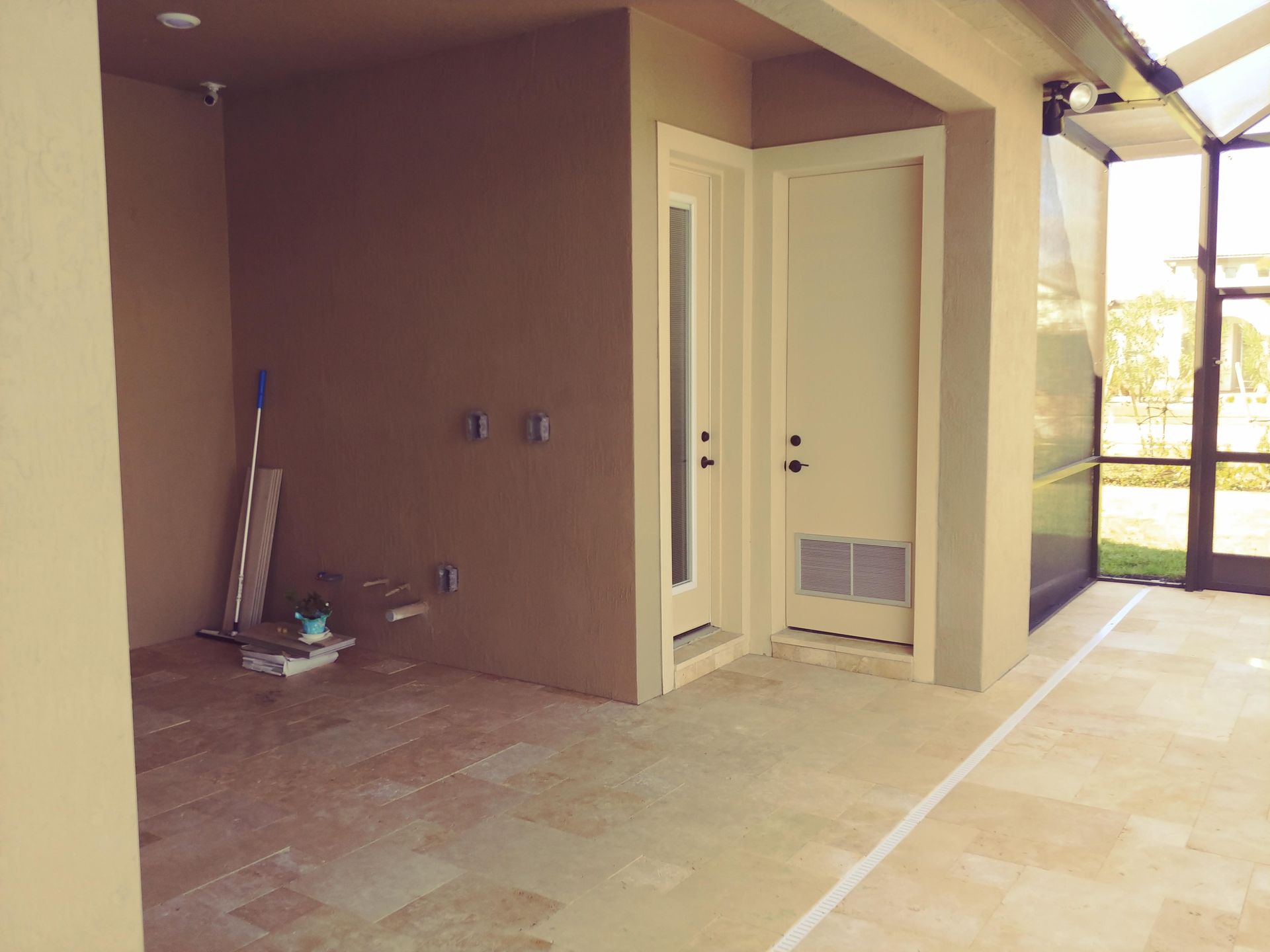 Partially finished patio with beige walls, tiled floor, and a small utility alcove door