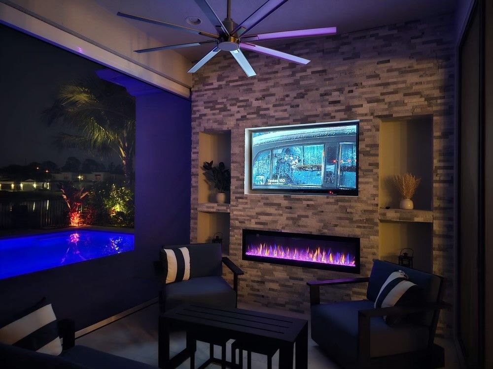 Modern patio lounge with a lit fireplace, ceiling fan, hot tub, and purple ambient lighting