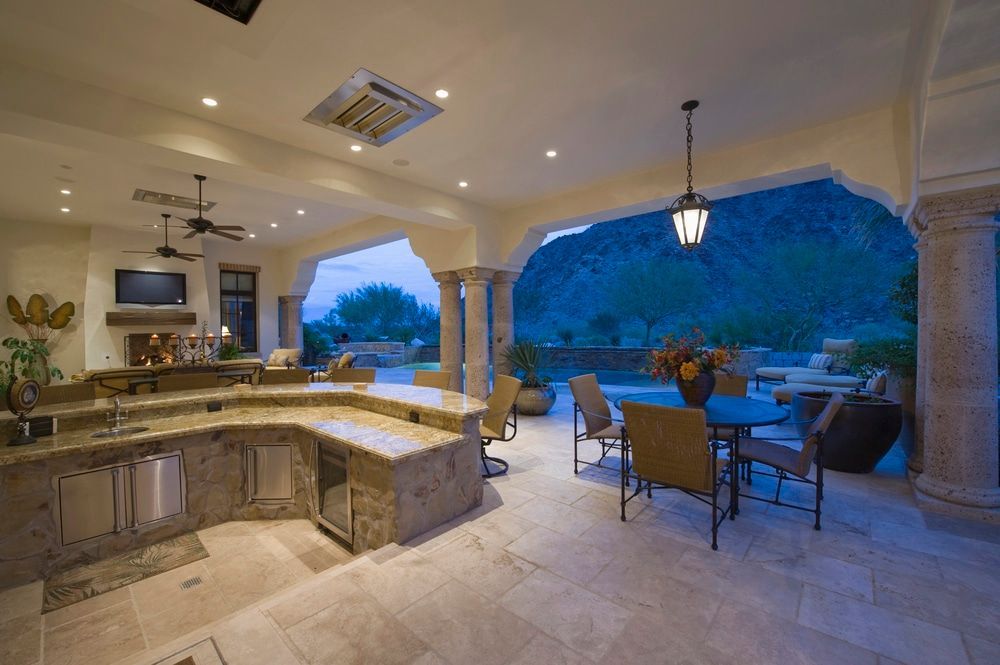 Luxurious covered patio with a stone kitchen, dining table, and ocean view at dusk
