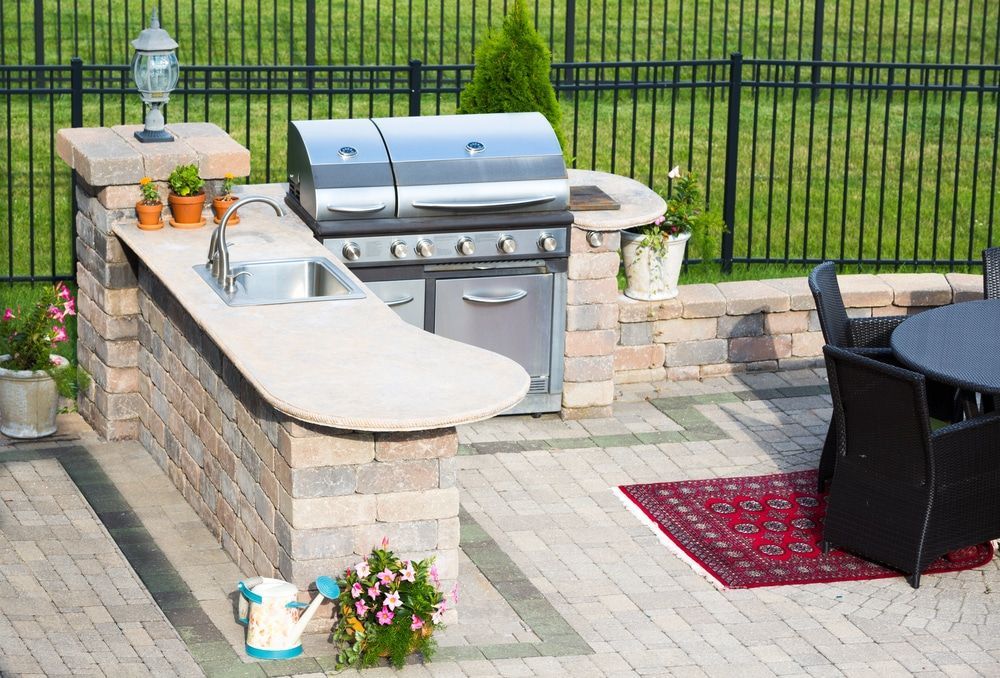 Outdoor patio with built-in grill, sink, stone counter, and black chair on a paver deck
