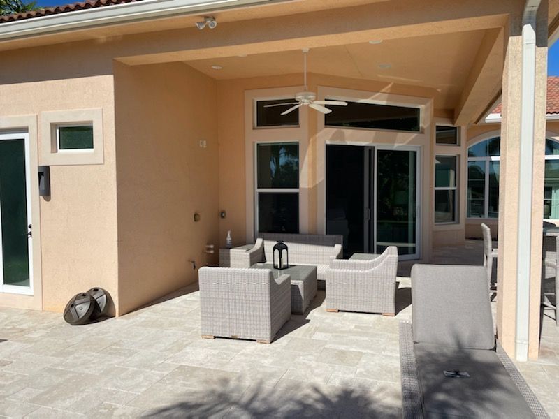 Covered patio with wicker seating and a sliding glass door beside a beige house