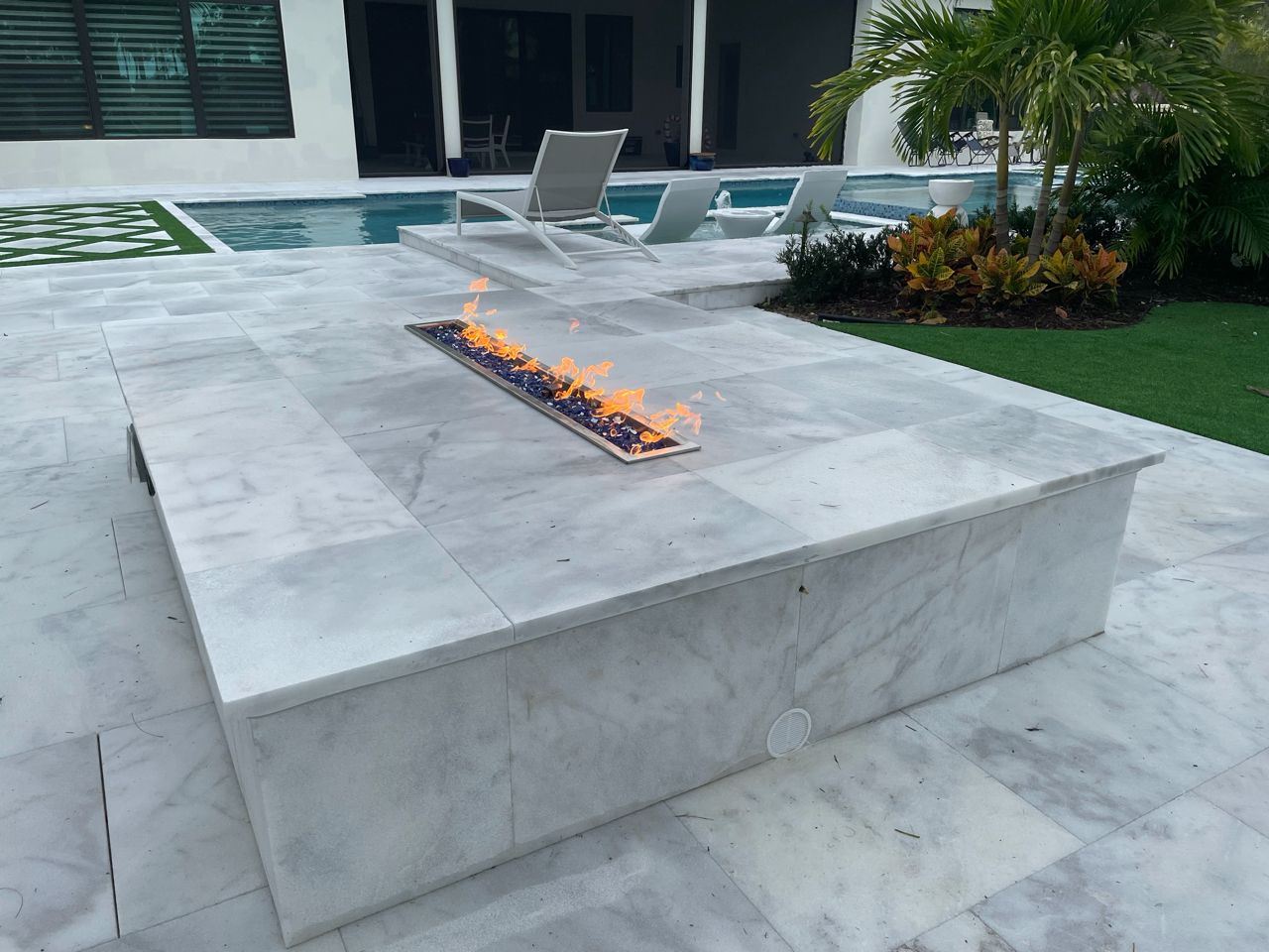 Modern patio with a built-in fire pit and lounge chairs beside a pool.