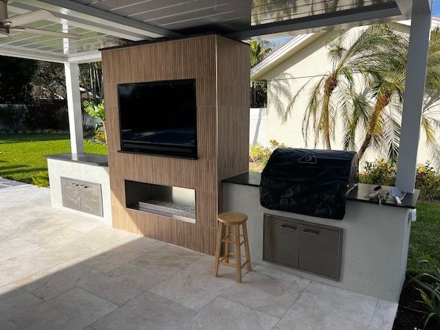 Outdoor covered patio with built-in TV, grill, and bar counter next to a wooden cabinet wall
