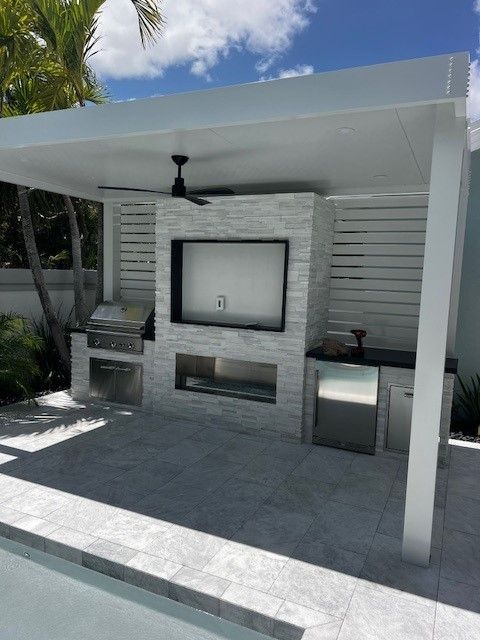 Outdoor covered patio with built-in grill, TV, ceiling fan, and gray tile flooring