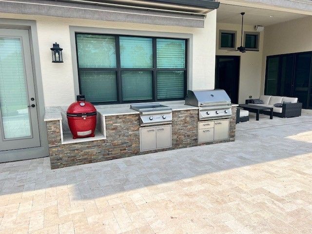 Patio with outdoor grill, red smoker, and sink beneath a window on a stone wall