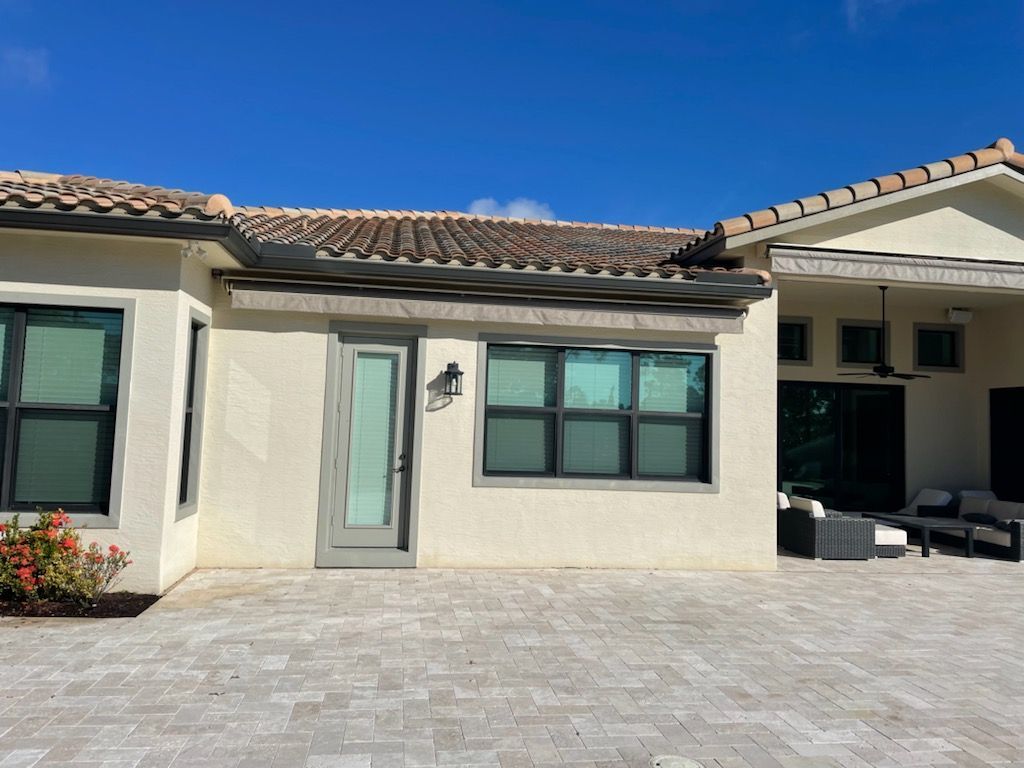 Modern stucco home exterior with gray door, black windows, and a tiled patio under a blue sky