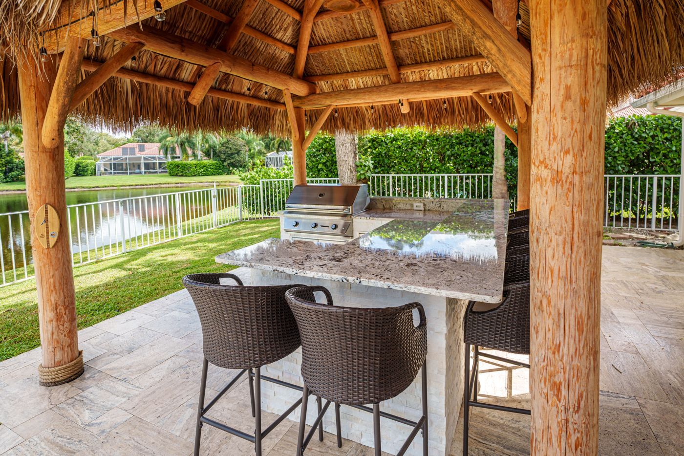 Covered patio with wicker chairs and dining table overlooking a garden pond and hedge