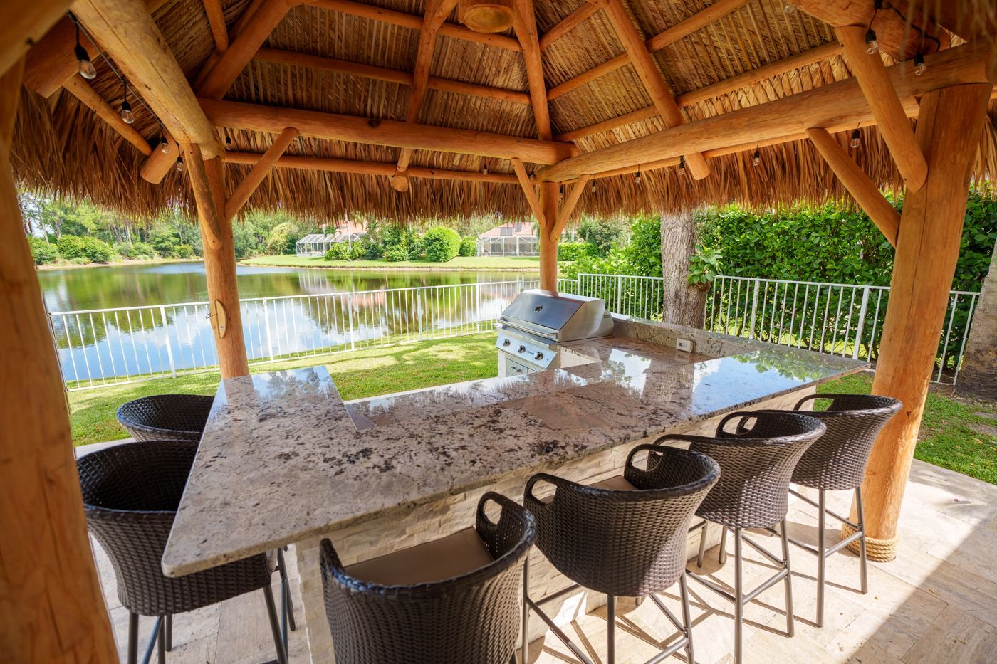 Tropical thatched-roof patio bar with granite counter, wicker stools, and poolside lagoon view