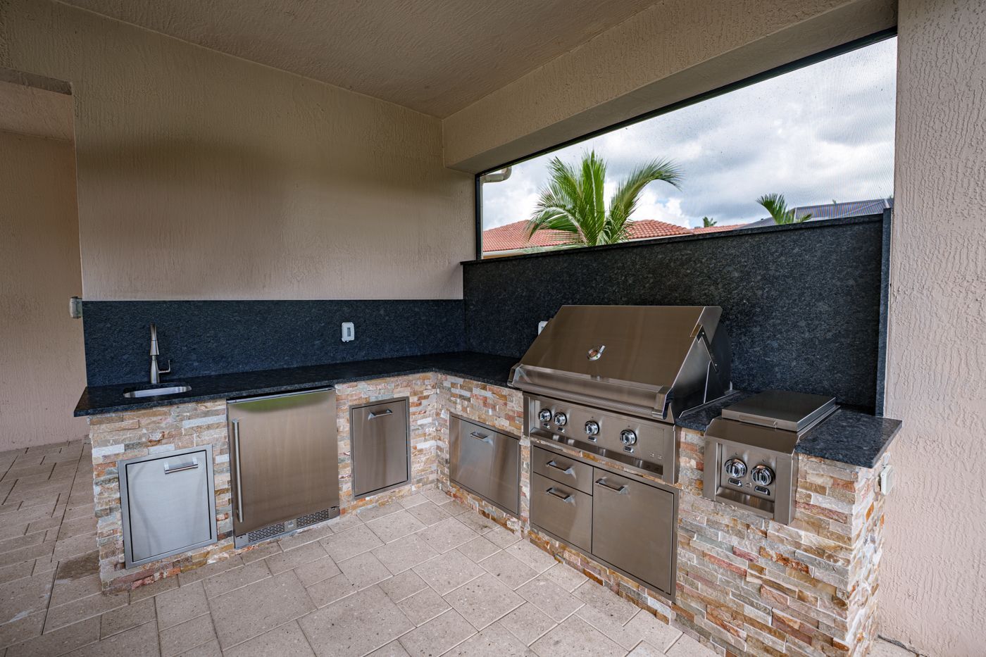 Outdoor patio kitchen with stainless grill, sink, and cabinets under a covered roof