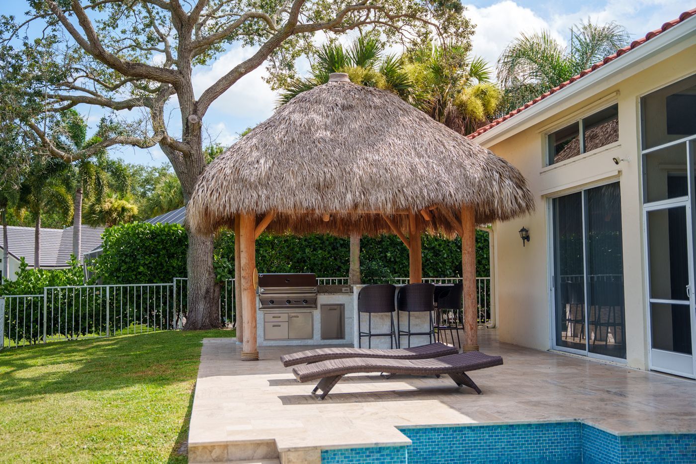 Backyard patio with thatched gazebo, picnic table, grill, and swimming pool beside a house