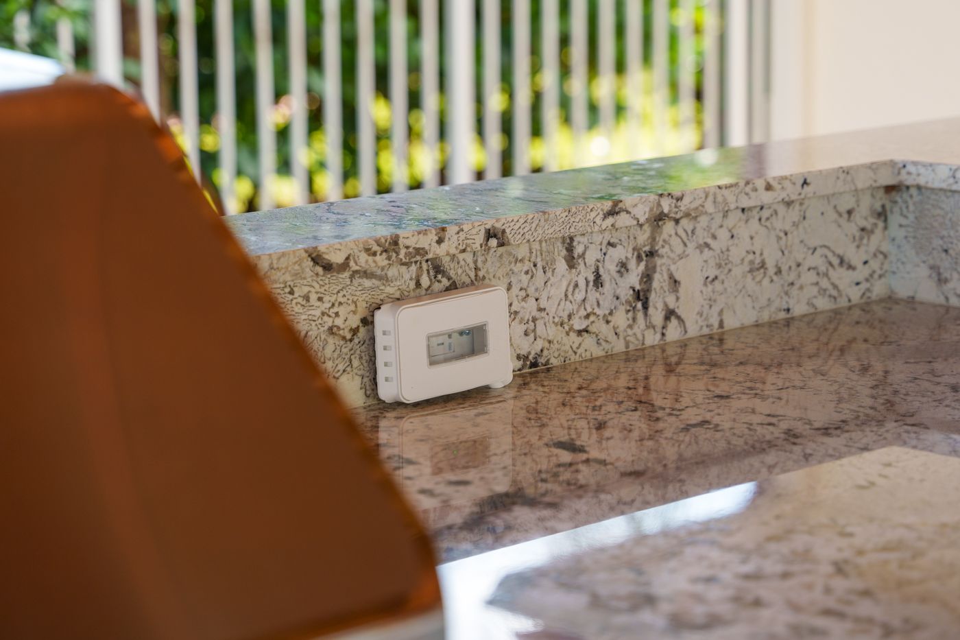 Granite countertop with a wall outlet and blurred balcony railing in the background