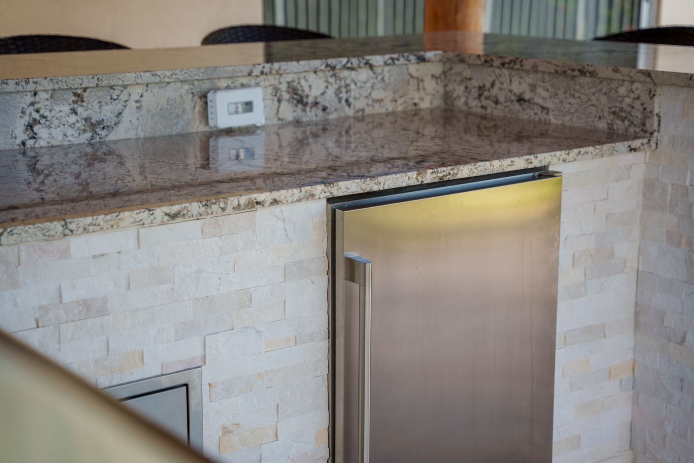 Stone kitchen counter and stainless-steel refrigerator with granite backsplash and light tile wall