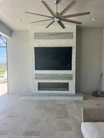 Modern covered patio with a wall-mounted TV, built-in fireplace, and ceiling fan.