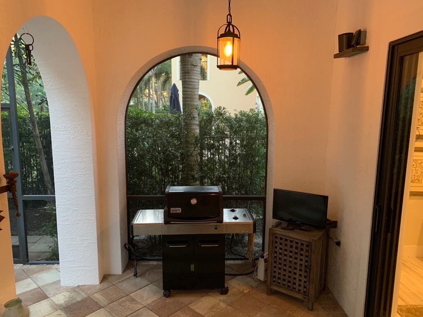 Covered patio with a grill, small TV, and arched openings overlooking greenery