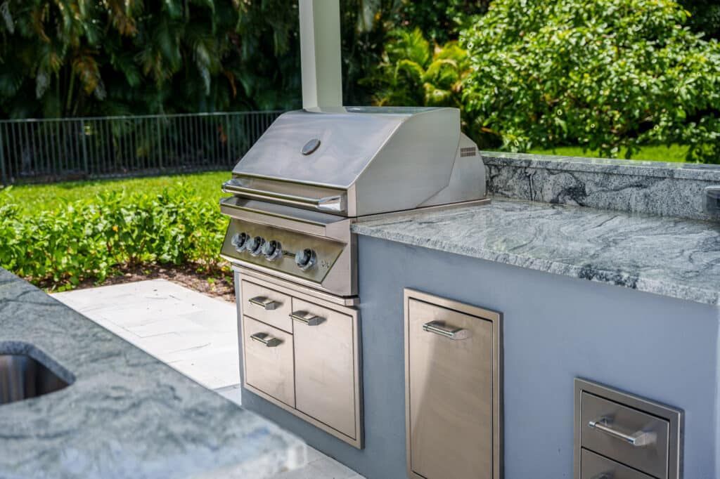 Built-in stainless steel grill with stone countertop in a backyard outdoor kitchen