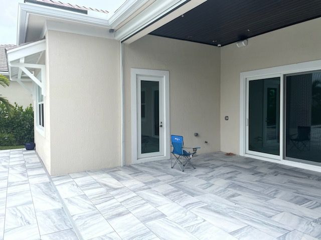 Covered patio with marble tile flooring, beige walls, and sliding glass doors, with a blue chair near the wall
