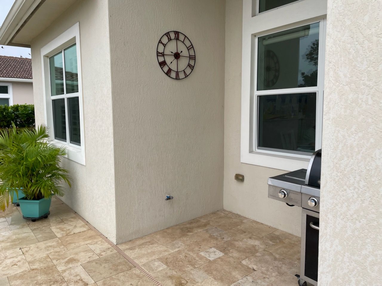Patio corner with wall clock, potted plant, windows, and a built-in grill on the right.