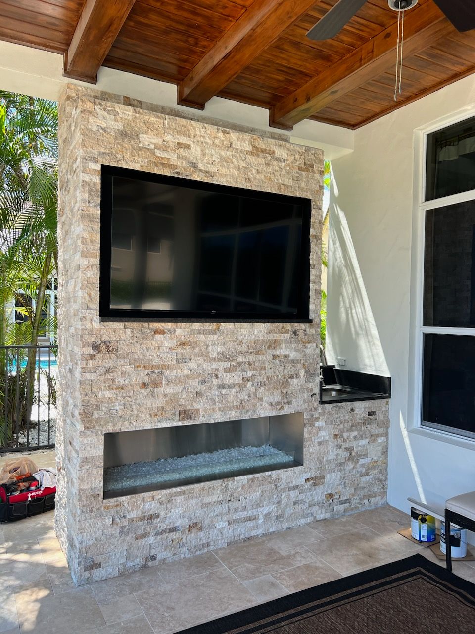 Stone outdoor fireplace with wall-mounted TV under a covered patio